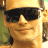 Pixelated close-up of a person wearing dark sunglasses and a light-colored cap, with a neutral expression against a blurred background.