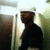 Pixelated static image shows a person in dark clothing standing outdoors with blurred background elements including vertical structures and light-colored sky.