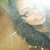 A pixelated image of a person with long dark hair and light skin, wearing a dark top against a brown background.