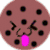 A circular brown cookie with black chocolate chips, a pink tongue sticking out, and two small black lines for eyes.