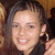 A woman with long dark hair and hoop earrings smiles in a pixelated image with a white and gray background.