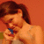 A pixelated image shows a person with brown hair holding a blue object near their mouth against an orange background.