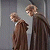 Pixelated static image of two human figures in brown robes standing side-by-side against a gray background, with visible facial features and clothing details.