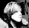 Black-and-white pixelated image of a person with short light-colored hair, side profile view showing shoulder-length strands and visible ear.