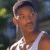 Pixelated image of a person wearing a white tank top and light-colored cap, set against blurred green and blue background elements.
