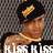 Pixelated image of a person with dark hair wearing a black cap and gold chain, standing against a checkered background.
