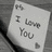 A grayscale image of a handwritten note reading 'I Love You' with a small heart symbol, displayed on a textured background.