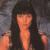 A pixelated image of a person with long dark hair and bangs, wearing a sleeveless top against a blurred background.