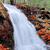 Static pixelated image of a waterfall flowing between rocky cliffs with green foliage above, rendered in low-resolution style.