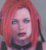 Pixelated portrait of a person with red hair, light skin, and dark eyes wearing a dark top against a muted background.