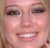 Pixelated close-up of a smiling person's face with light brown hair visible on the left side, showing eyes, nose, mouth, and cheeks.
