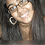 A person with long dark hair and hoop earrings smiles broadly, wearing glasses in a split- view