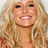 Pixelated close-up of a person with long wavy blonde hair, light skin tone, and visible teeth in a smiling expression.