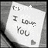 A pixelated grayscale image of a white card with handwritten text "I love you" and a small heart symbol, set against a dark background.