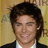 Static pixelated image of a person with dark hair wearing a dark jacket over a white shirt against a light brown background.