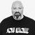 Pixelated grayscale image of a person with a bald head, closed eyes, and a goatee, wearing a black shirt with white text.