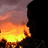 Silhouette of a figure against fiery background with orange and yellow flames, purple sky, and black borders.