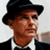 Pixelated close-up of a person wearing a black fedora, dark suit jacket, white shirt, and black bow tie against a light background.