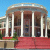 Static image of a classical building facade with columns, red carpeted steps, and blue sky background.