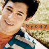 A person with dark hair wearing a blue and white striped shirt over an orange undershirt, lying on a textured surface with the word 'broy' in pixelated text.