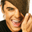 A pixelated close-up of a person with brown hair smiling broadly, hand near face, wearing black shirt; cyan 'G' symbol appears on right side.