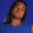 Pixelated portrait of a person with long dark hair against solid blue background, wearing light-colored top.