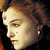 Pixelated close-up of a person's face with light skin, brown hair, and a small red mark on the cheek, set against a dark background.