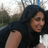 A pixelated static image shows a person with long dark hair wearing a black top, positioned against an outdoor background with blurred greenery and light-colored structures.
