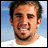 Pixelated image of a person with short brown hair and a goatee, wearing a white shirt against a blue sky background, with text on pink and gray