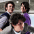 Three people in formal attire stand close together; one wears a dark suit with blue accents, another purple clothing, and the third gray with black details.