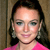 A pixelated close-up of a person with dark hair, wearing a bright pink top and large earrings, against a neutral-toned background.