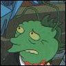 Green-skinned cartoon character with large yellow eyes, downturned mouth, and dark hair, wearing a red bow tie and white shirt collar.