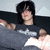 Pixelated static image of a person with dark hair wearing a dark shirt, extending an arm toward the viewer against a light background.