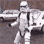 Animated sequence of a stormtrooper figure in white armor holding a blaster rifle, standing before two parked cars on a street.