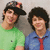 Two figures in green and blue shirts with red ties, wearing hats, positioned side-by-side against a neutral background.