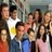 Group of people in casual clothing standing closely together, some with arms raised or crossed.