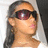 Pixelated close-up of a person with long dark hair wearing dark sunglasses and a light-colored top against a light background.