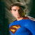 A pixelated image of a female figure in blue with a red and yellow emblem on her chest, next to a standalone red shield-shaped logo with the same emblem.