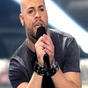 A person in a dark gray striped shirt holds a black microphone with both hands, wearing a black wristband on the right wrist.
