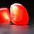 Two red, glossy, rounded objects with light reflections on a dark background, one partially overlapping the other.