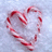 A heart-shaped arrangement of red and white striped candy canes on a light blue pixelated background.