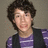 Pixelated portrait of a person with dark curly hair wearing a purple striped shirt and dark vest against a neutral background.