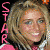 Pixelated image of a smiling person with light brown hair wearing pink and white clothing, vertical pink text on left side.