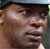 Pixelated static image of a person's face with dark hair and light skin tone, wearing a dark cap or head covering, against a neutral background.