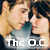 Two side-by-side figures in a close embrace, one with light brown hair and the other with dark hair, both wearing blue tops, with text below reading The O.C.