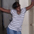 Pixelated image of a person in a white striped shirt and blue pants with arms raised against a light-colored wall.