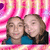 Two people with brown hair pose closely together against a pink and white striped background with a purple heart shape in the top left corner.