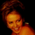 Pixelated static image of a person with curly hair against black background, warm orange-brown color palette, low-resolution rendering.