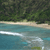 Pixelated beach scene with turquoise water, white wave, sandy shore, and dense green foliage background.