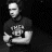 Static grayscale pixel art of a person in a dark shirt with indistinct text on the chest, making a thumbs-up gesture against a black background.